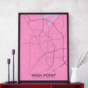 Può includere: Una mappa rosa incorniciata di High Point, Carolina del Nord, Stati Uniti. La mappa è in una cornice nera e ha uno sfondo bianco con linee nere che mostrano le strade. Il testo "HIGH POINT" è stampato in nero nella parte inferiore della mappa.