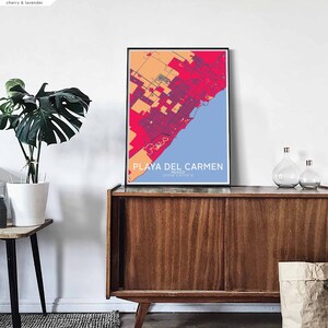Puede incluir: Una impresi&oacute;n de mapa colorido de Playa del Carmen, M&eacute;xico, en un marco negro, colgado en una pared blanca sobre un gabinete de madera. El mapa est&aacute; en tonos de rojo, naranja y azul.
