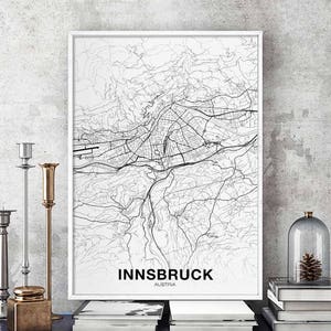 May include: Black and white map print of Innsbruck, Austria. The map shows the city streets and surrounding area. The print is framed in a white frame and is hanging on a wall.