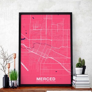 May include: A black framed print of a pink map of Merced, California, United States. The map shows the city's streets and roads.