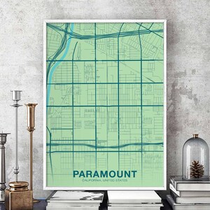 Puede incluir: Una impresión de mapa verde y azul de Paramount, California, Estados Unidos. El mapa está enmarcado en un marco blanco y se muestra en un estante con libros y velas.