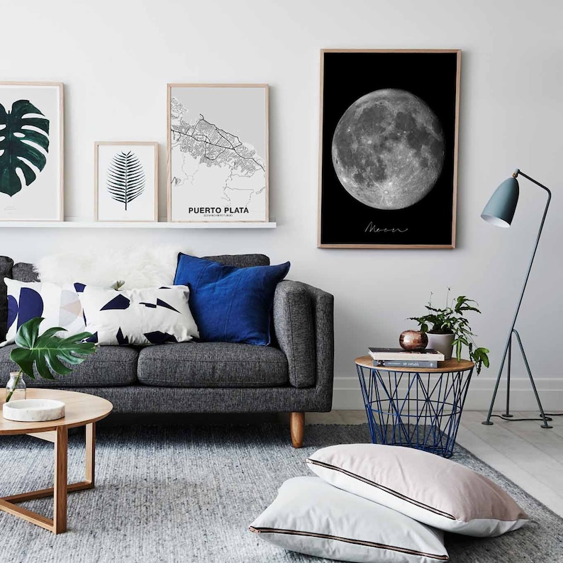 Puede incluir: Un interior de sala de estar con un sof&aacute; gris, una mesa de caf&eacute; y una mesa auxiliar con una cesta de alambre. Las paredes son blancas y hay varias impresiones enmarcadas en la pared, incluyendo una foto en blanco y negro de la luna y un mapa de Puerto Plata. El sof&aacute; tiene almohadas azules y blancas.