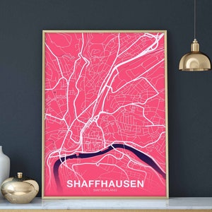 May include: A pink and white map print of Schaffhausen, Switzerland, in a gold frame. The map shows the city's streets and waterways.