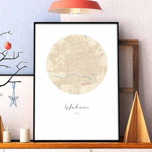 Op de afbeelding: Een zwart ingelijste print van een cirkelvormige kaart van Isfahan, Iran. De kaart is in beige tinten met een witte achtergrond. De naam van de stad staat in cursief onder de kaart.