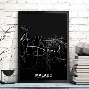 Puede incluir: Impresión en blanco y negro de un mapa de la ciudad de Malabo, Guinea Ecuatorial, en un marco negro. El mapa está sobre un fondo de pared de ladrillo blanco.