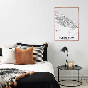 Puede incluir: Una impresi&oacute;n de mapa en blanco y negro de Puerto Plata, Rep&uacute;blica Dominicana, en un marco de oro rosa, colgada en una pared blanca sobre una cama con ropa de cama blanca, una manta de lana marr&oacute;n y almohadas a rayas blancas y negras.