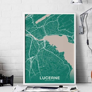 May include: A framed map print of Lucerne, Switzerland, in a teal and beige color scheme. The map features white lines representing roads and streets, with the city's name and country at the bottom. The print is displayed on a white surface.