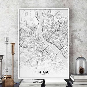 Op de afbeelding: Een zwart-witte kaartprint van Riga, Letland, in een wit frame. De kaart toont de straten en waterwegen van de stad. De naam van de stad en het land zijn onder de kaart afgedrukt.