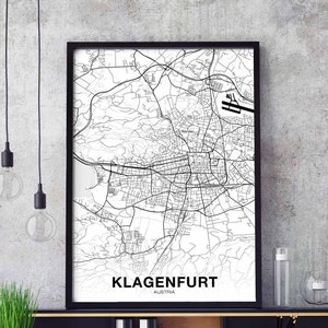 May include: Black and white framed map print of Klagenfurt, Austria. The detailed city map shows streets, roads, and an airport. The city name and country are printed in a clean, modern font at the bottom of the print.