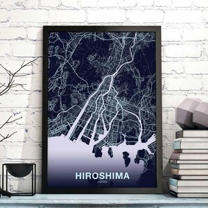 Puede incluir: Una impresión enmarcada en negro de un mapa de Hiroshima, Japón. El mapa está en azul y blanco y muestra las calles y vías fluviales de la ciudad. El texto "HIROSHIMA" está impreso en blanco en la parte inferior del mapa.