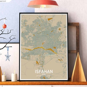Op de afbeelding: Een beige en blauwe kaartprint van Isfahan, Iran, met een gouden rivier en stadsdetails. De print is ingelijst in een zwart frame en wordt tentoongesteld op een plank met decoratieve ornamenten.