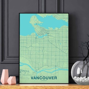Può includere: Una stampa di mappa di Vancouver, Canada, incorniciata in nero. La mappa è di colore verde chiaro con elementi d'acqua blu. Il nome della città è stampato in bianco nella parte inferiore della mappa.