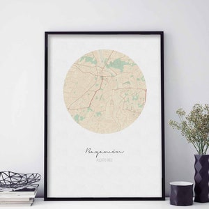 May include: A black framed print of a map of Bayamón, Puerto Rico. The map is in a circle and is beige with green accents. The city name is written in cursive below the map.