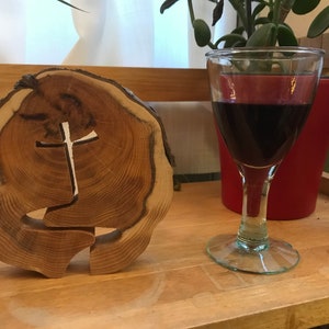 Może przedstawiać: Drewniany wycięty krzyż na drewnianym plastrze z kieliszkiem czerwonego wina w tle.