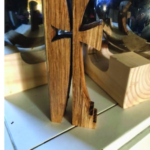 May include: A wooden cross with a Celtic knot design, standing on a wooden base. The cross is made of dark wood with a light wood grain.