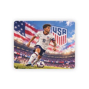 Peut inclure: Un puzzle rectangulaire représentant un joueur de football en maillot blanc avec le numéro 10, un short bleu foncé et des chaussettes blanches, dribblant un ballon sur un terrain. Le fond montre un stade, un grand drapeau USA et un écusson USA.