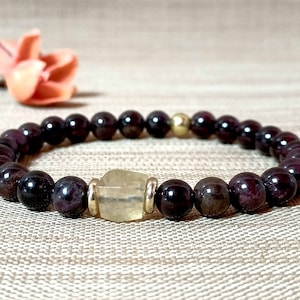 Peut inclure: Un bracelet de pierres précieuses rouge foncé avec une seule perle de pierre précieuse jaune clair et des accents dorés.