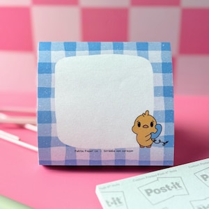 May include: Square Post-it note pad with a blue gingham border and a blank white center. A cartoon chick holding a blue telephone is on the right. The text "Pekita Paper Co. | Scribble con corazon" is at the bottom.