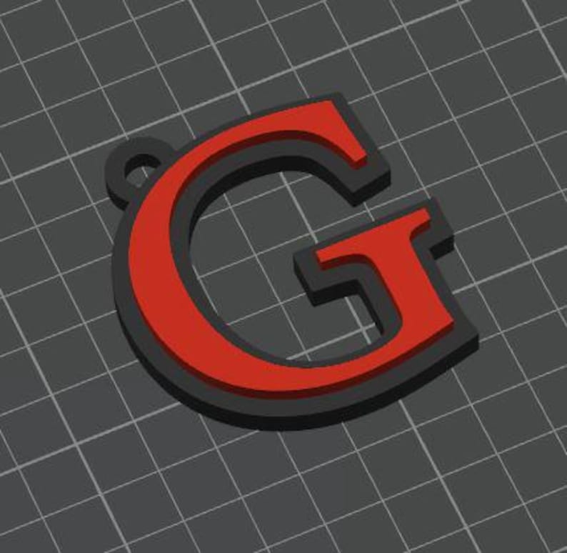 May include: A three-dimensional letter G pendant featuring a bold red face layered over a solid black base. The letter has a serif typeface design with a small circular loop at the top left corner for attachment, presented against a dark gray grid.