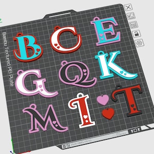 Könnte beinhalten: Eine Sammlung von 3D-gedruckten Buchstaben und herzförmigen Anhängern. Die Buchstaben sind in verschiedenen Farben wie Blau, Rot, Weiß, Rosa und Schwarz gehalten und mit Herzakzenten versehen. Sie liegen auf einer strukturierten PEI-Platte.