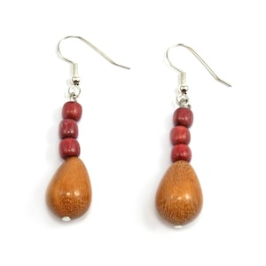 May include: A pair of wooden earrings with a teardrop shape. The earrings are made of brown wood with red wooden beads. The earrings have silver hooks.