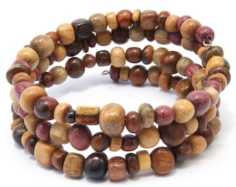 Puede incluir: Un brazalete de madera de varios niveles con cuentas marrones, moradas y beige. El brazalete está hecho de madera natural y tiene un aspecto rústico.