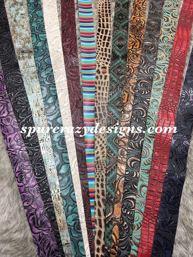 May include: A collection of 16 different leather straps with various embossed patterns and colors, including floral, geometric, and animal prints. The straps are arranged in a vertical row and are all approximately 1 inch wide. The text "spurcrazydesigns.com" is visible at the bottom of the image.