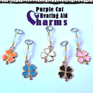 May include: Five gold-colored four-leaf clover charms with different colored enamel centers: orange, white, blue, black, and pink. Each charm is attached to a silver ring with a crystal bead and a gold bead.