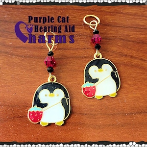 May include: Two gold penguin charms with red strawberries and black glitter. The charms are attached to gold jump rings with black and red beads. The charms are for hearing aids.