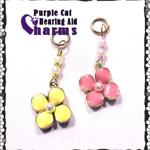 May include: Two gold flower charms with pearl centers. The flower on the left is yellow and the flower on the right is pink. Both charms have a gold jump ring and a string of white pearls.