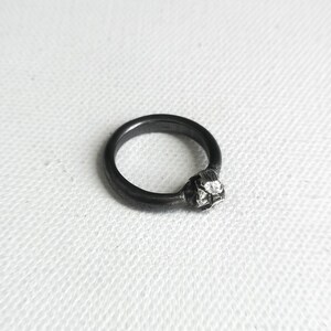 May include: A black metal ring with a small, textured, silver-colored stone.