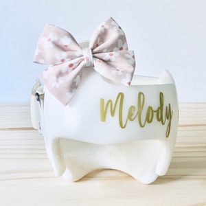 May include: White padded helmet with a pink floral bow and the name "Melody" written in gold lettering.