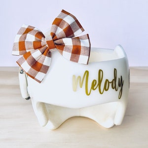 May include: White helmet with a brown and white gingham bow and the name "Melody" written in gold lettering.