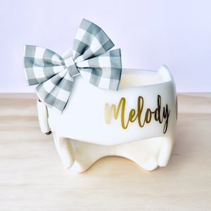 May include: White helmet with a gray and white gingham bow and the name "Melody" written in gold lettering.
