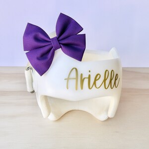 May include: White helmet with a purple bow and the name "Arielle" written in gold lettering.
