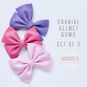 May include: Set of three fabric hair bows in purple, pink, and light pink. The bows are handmade and are labeled "Cranial Helmet Bows Set of 3" and "Handkrfted Handmade by Katrina Rose".