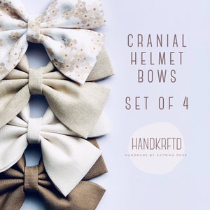 May include: Set of four handmade fabric bows in beige, brown, and white with a floral print. The bows are arranged in a stack and labeled "Cranial Helmet Bows Set of 4" and "HANDKRAFTD Handmade by Katrina Rose".