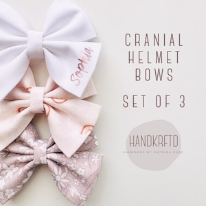 May include: Set of three handmade fabric bows for a cranial helmet. The bows are in shades of pink and white with a floral pattern, a rainbow pattern, and a white bow with the name "Sophia" embroidered on it.