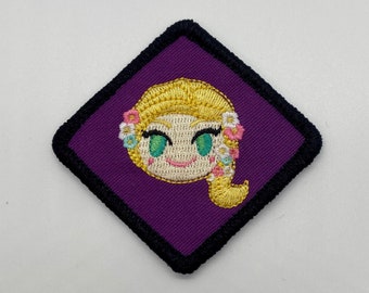 Op de afbeelding: Paarse geborduurde patch met een cartoonfiguur met geel haar, groene ogen en een roze bloemenkrans. Het personage glimlacht en heeft een gele vlecht.