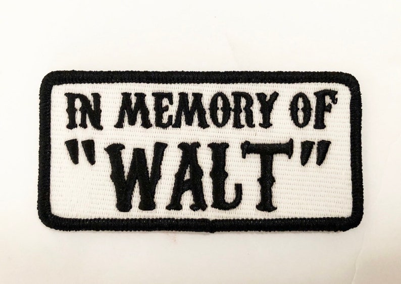 Op de afbeelding: Witte geborduurde patch met zwarte stiksels. De patch heeft de tekst "In Memory of "Walt""