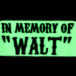 Op de afbeelding: Een groene patch die in het donker gloeit met zwarte geborduurde tekst die "In Memory of "Walt" luidt.