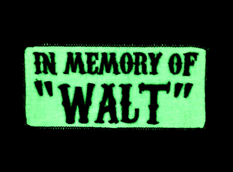 Op de afbeelding: Een groene patch die in het donker gloeit met zwarte geborduurde tekst die "In Memory of "Walt" luidt.