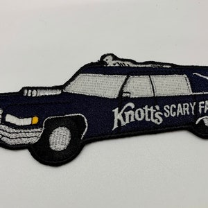 May include: A black and white embroidered patch of a hearse with a skeleton on the roof. The hearse has the text "Knott's Scary Farm" on the side.