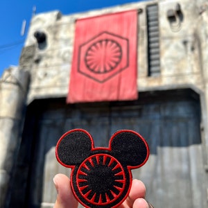 May include: A black and red embroidered patch shaped like Mickey Mouse's head with the Star Wars First Order symbol in the center.