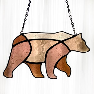 May include: A stained glass bear silhouette with brown and beige glass pieces. The bear is hanging from a black chain.