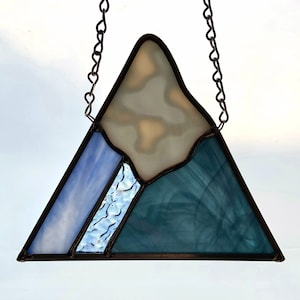 K&ouml;nnte beinhalten: Eine Berglandschaft aus Buntglas mit einem hellblauen, wei&szlig;en und dunkelblauen Design. Der Berg h&auml;ngt an einer silbernen Kette.
