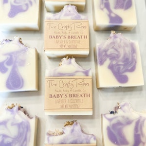 Op de afbeelding: Meerdere handgemaakte zeepstaven met een paarse en witte swirl-ontwerp. De zeep is gelabeld "The Crafty Roses Bath, Body & Candle Co. Baby's Breath Lavender & Chamomile Net Wt. 4 oz (113g)"