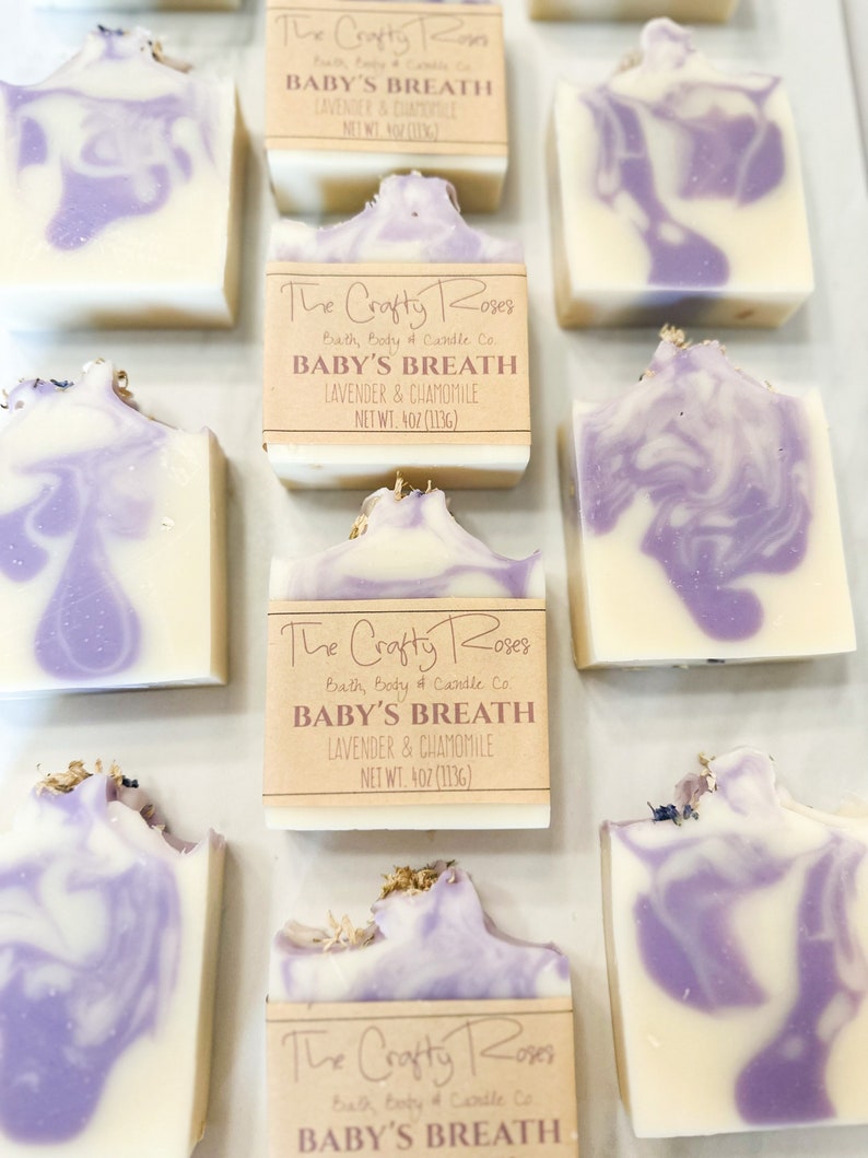 Op de afbeelding: Meerdere handgemaakte zeepstaven met een paarse en witte swirl-ontwerp. De zeep is gelabeld "The Crafty Roses Bath, Body & Candle Co. Baby's Breath Lavender & Chamomile Net Wt. 4 oz (113g)"