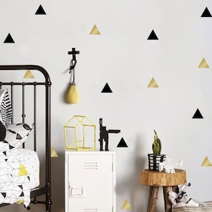 Peut inclure: Un mur blanc avec des autocollants muraux en forme de triangles noirs et dorés. Le mur est dans une pièce avec un lit, une table de chevet, une plante et un tabouret.