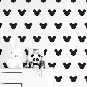 Puede incluir: Una pared blanca con un patrón repetitivo de orejas de Mickey Mouse negras. La pared está decorada con un cuadro enmarcado que dice "Feliz cumpleaños" y una ilustración de un panda.
